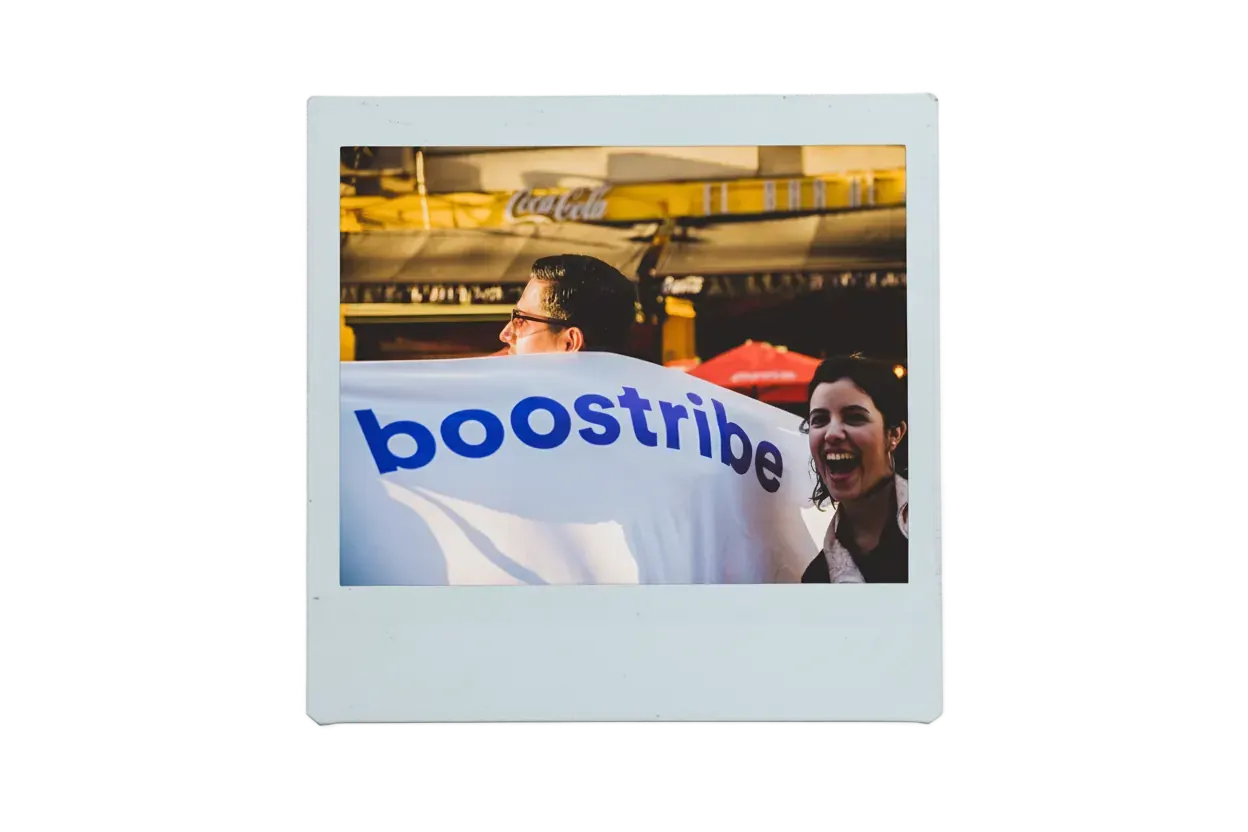 Dos personas en la calle sostienen una bandera blanca con el logo de boostribe; una de ellas se ríe